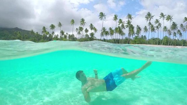 UNDERWATER: Young man in swimsuit swimming in perfect island lagoon