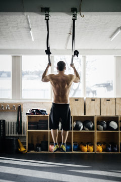Rear view of young man exercising on gymnastic rings in gym