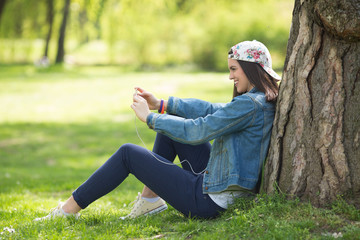 Teenage girl is relaxing in a park and using smart phone.