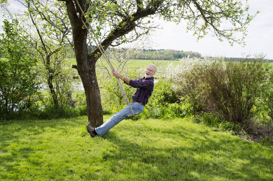 Side view of smiling senior man sitting on swing