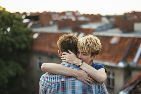 Germany, Berlin, Young couple hugging on rooftop at sunset