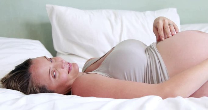 Pregnant woman touching her belly on bed