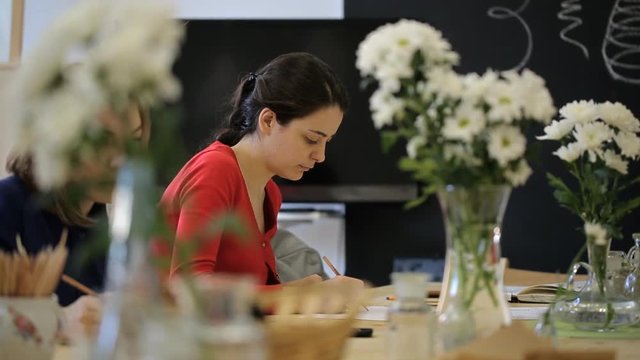 Young woman in red blouse draws white flowers in a vase.