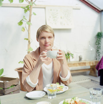 Woman holding cup of coffee and having breakfast on the table