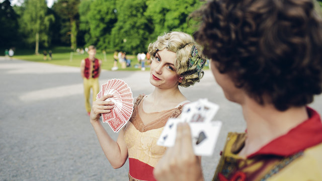 Young circus performers holding playing cards in park