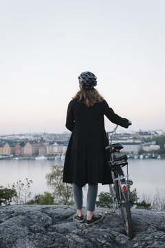 Sweden, Sodermanland, Stockholm, Sodermalm, Skinnarviksberget, Rear view of young woman standing by bicycle on rock