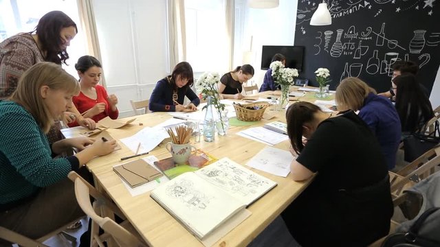 People sit around wooden table in art studio on seminar.