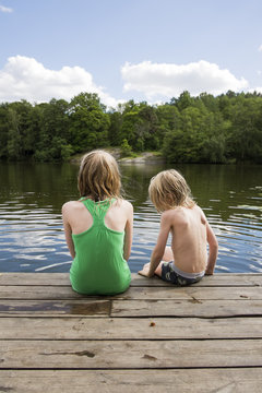 Sweden, Stockholm, Nacka, Sicklasjon, Lake Sickla, Rear view of children (6-7, 10-11) sitting on wooden jetty