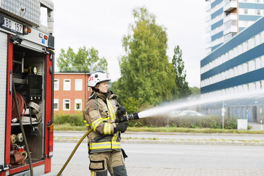 Sweden, Sodermanland, Sodertalje, Female firefighter using fire hose next to truck