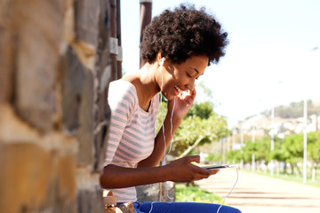 Smiling woman with mp3 player sitting in park