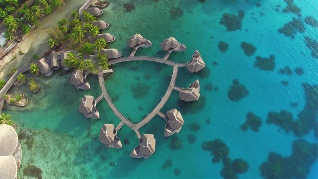 AERIAL: Luxury overwater villas on jetty above the ocean lagoon