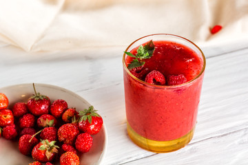 glass of berry smoothie, plate with raspberries and strawberries