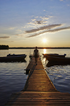 Sweden, Vastra Gotaland, Skagern, Woman walking on pier in lake at sunset