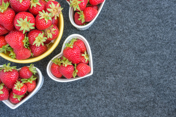 Fresh picked strawberries in a yellow bowl, and white heart shaped bowls, on a gray background
