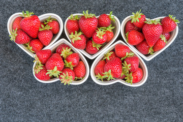 Fresh picked strawberries in white heart shaped bowls, on a gray background
