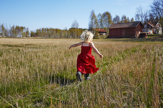 Sweden, Vastra Gotaland, Gullspang, Girl (4-5) wearing red dress running in field