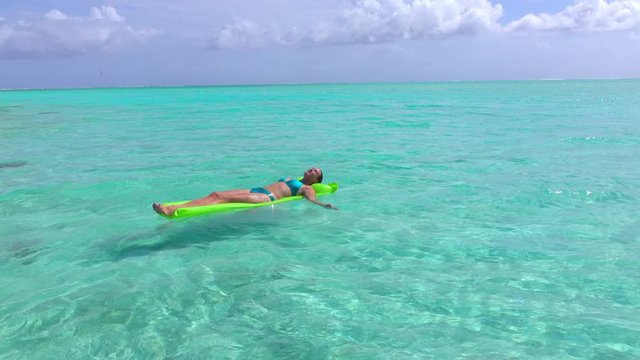 Woman relaxing on inflatable air mattress in beautiful blue lagoon