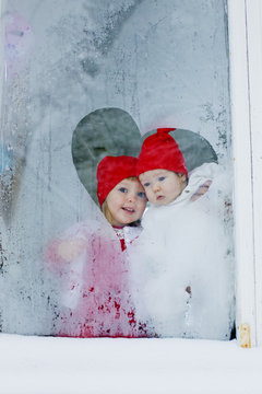 Girl (2-3) and her baby sister (12-17 months) looking out frosted window