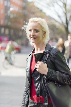 Sweden, Uppland, Stockholm, Young woman standing on sidewalk, smiling