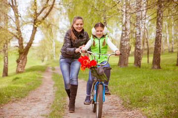 happy mother teaches his daughter to ride a bike. Mother holds daughter from falling