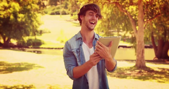 Handsome man using tablet and laughing in the park