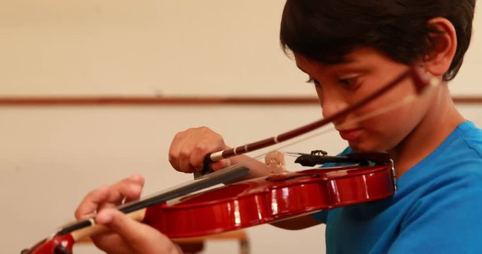 Cute pupil playing violin in classroom