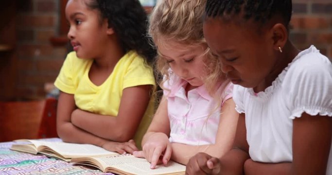 Cute pupils reading books at desk in elementary school