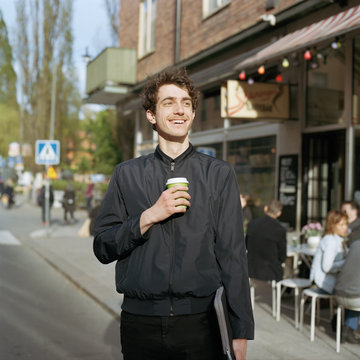 Sweden, Stockholm, Sodermalm, Nytorget, Smiling man standing on street with laptop and disposable cup in hand