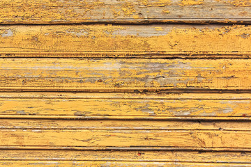 Grunge wood wall with cracks and peeling paint in old house. Yellow textured background.