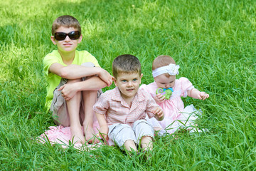 Three children sit in grass, playing and having fun.