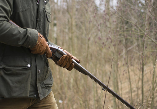 Midsection of hunter with rifle walking in forest