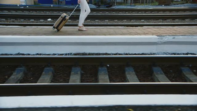 A woman in a business suit in a travel bag is on the railway station. In the picture can be seen only the legs and a bag on wheels