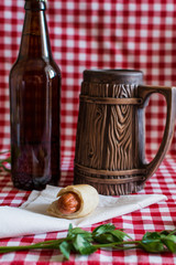 Homemade Mini hot dog (sausage in pastry) on napkin with a bottle of dark beer and earthenware mug on a plaid background