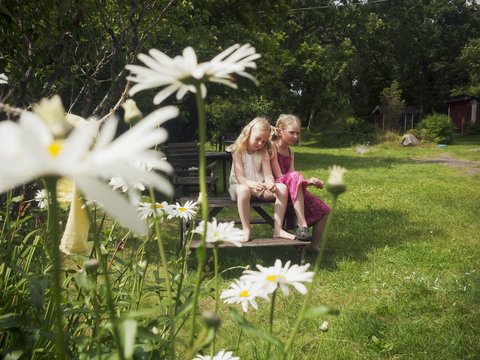 Sweden, Smaland, Two girls (6-7, 7-8) sitting on wooden bench in domestic garden