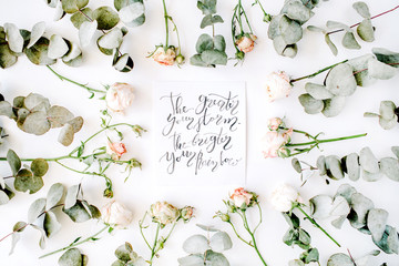 inspirational quote the greater your storm the brighter your rainbow written in calligraphy style on paper with pink roses and eucalyptus branches on white background. flat lay, top view