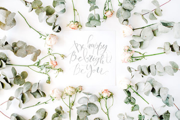 inspirational quote be happy, be bright, be you written in calligraphy style on paper with pink roses and eucalyptus branches on white background. flat lay, top view.