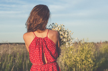 Back of charming girl with a bouquet of daisies in field