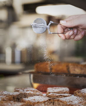 Woman's hand sifting powdered sugar over pieces of cake