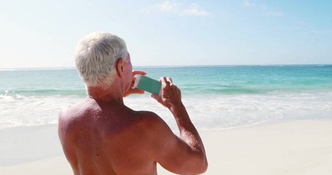 Retired old man standing while taking pictures on the beach
