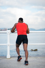Male runner stretching towards the sea for warming up before running. Black athlete exercising.