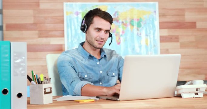 Casual businessman using laptop and having conversation with headset