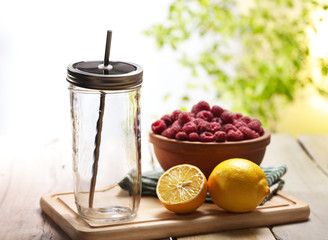 Beverage preparation. On wooden boards is clear jar glass with steel straw and lemon and raspberry bowl. Country ice cold drink beverage stewed fruit number hundred twenty five with raspberry outdoor.
