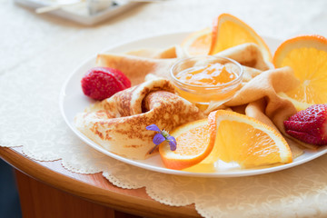 Closeup plate with pancakes with pieces of oranges, strawberries and jam bowl