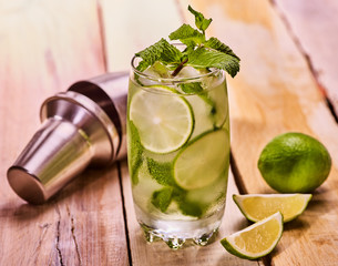 Alcohol drink. On wooden boards glass with alcohol drink and ice cubes. A drink number hundred eight cocktail mohito with cocktail shaker and mint leaf. Country life. Light background.