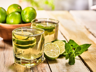 Country drink. On wooden boards are two glasses with green transparent drink and lime glue bowl. Drink number hundred four mojito with mint leaf on sunlight . Country life. Light background.