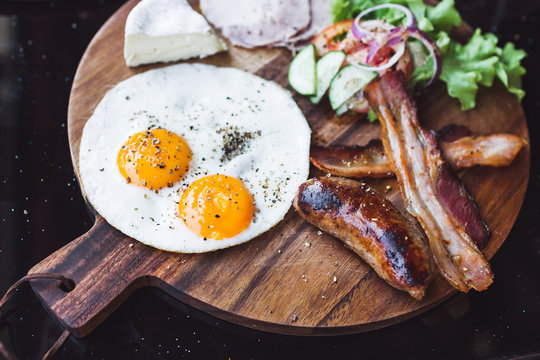 Breakfast with fried eggs, bacon and cheese camembert on wooden