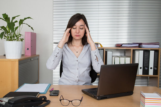 Exhausted businesswoman in her office with head in hands