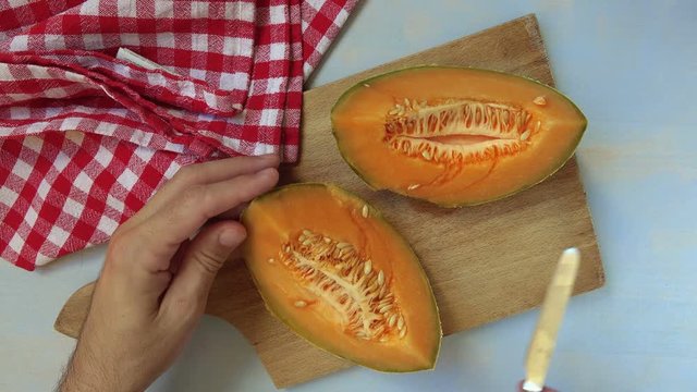 Man slicing tasty cantaloupe melon on table, top view of male hands with rustic kitchen knife cutting fruit.