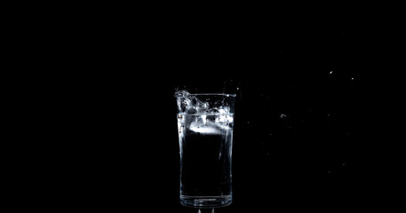 Ice landing in glass of water making a splash
