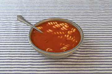 Rotini tomato soup in a bowl on a striped tablecloth